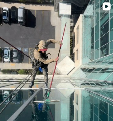 Pro window cleaner squeegeeing a glass facade from above